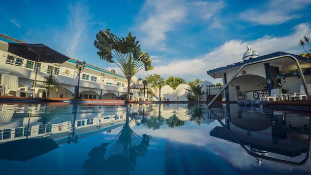 A hotel with a swimming pool reflecting the buildings and palm trees, a covered area with seating, and a dome structure. - Hotel Paraíso Kora (Aticama)