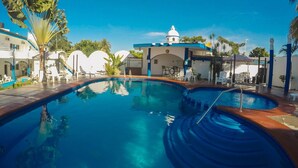 A swimming pool with two distinct sections, surrounded by lounge chairs and umbrellas, with a building featuring a dome and blue accents in the background. - Hotel Paraíso Kora (Aticama)