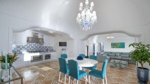 A spacious living area with a round dining table, teal chairs, and a chandelier. - Villa Aisha Private jacuzzi pool in Praiano (Praiano)