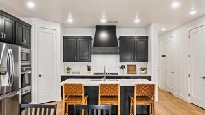 Eine moderne Küche mit dunklen Schränken, einem Edelstahl-Kühlschrank, einem Backofen und einer zentralen Kochinsel mit Sitzgelegenheiten.