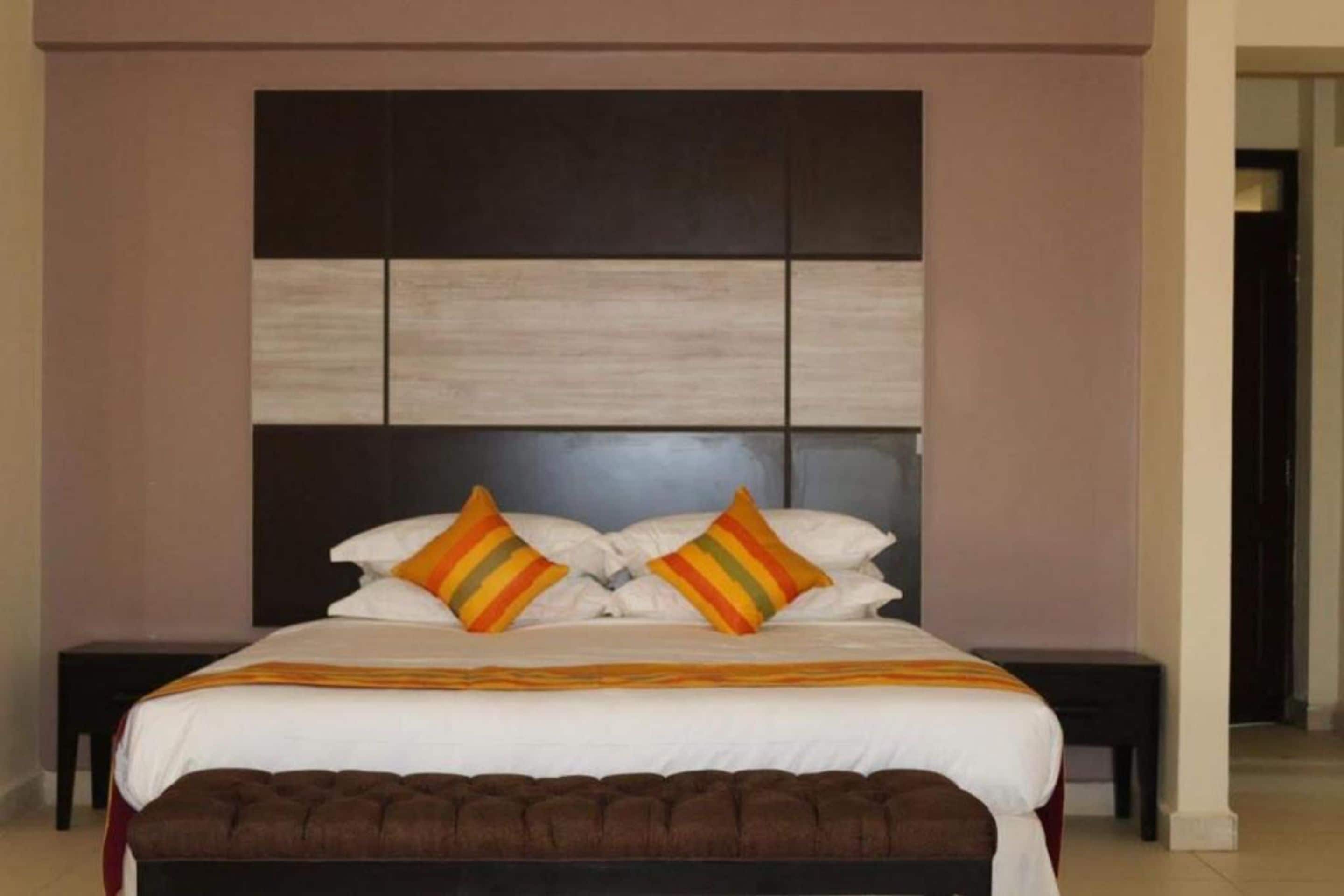 A neatly made bed with white linens and striped pillows, a brown upholstered bench, and a wooden headboard.