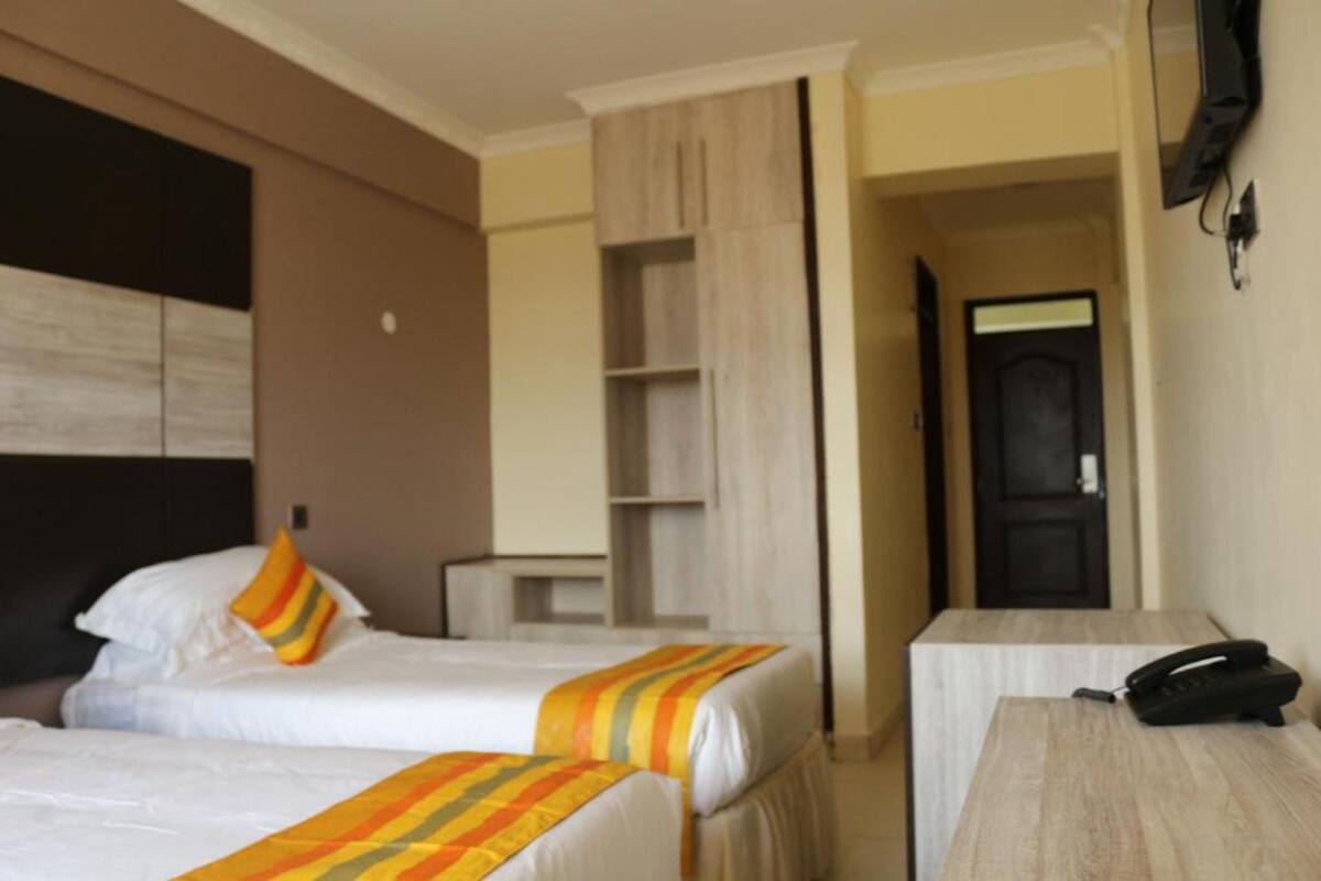 A hotel room with two beds, a desk, a telephone, and a television mounted on the wall.