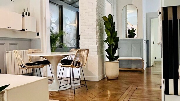 A modern kitchen with white brick walls, wooden flooring, and a dining area with two chairs and a table. - ✨ Luxury 2BR - 300m from Eiffel Tower - Rue Cler area (Paris)