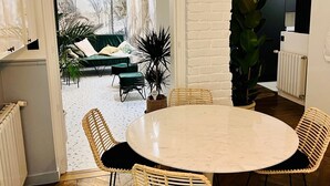 A dining area with a round table and wicker chairs, a white brick wall, and a view of a garden with a sofa and plants. - ✨ Luxury 2BR - 300m from Eiffel Tower - Rue Cler area (Paris)