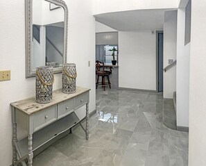 A hallway with a marble floor, a white wall, a mirror, and a wooden dresser with decorative vases. - "Lake house w/Mountain views” near River & Casinos (Bullhead City)