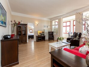 Un salon spacieux avec un plancher en bois, un canapé rouge, une table basse, un téléviseur et une bibliothèque.