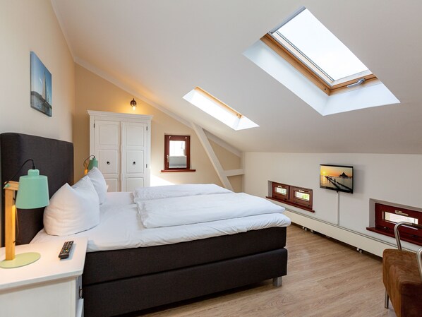 Une chambre à coucher comprenant un lit, un bureau, une chaise, un téléviseur et deux fenêtres de toit.