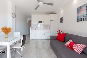 A modern living space with a dining area, kitchenette, and a gray sofa with red pillows.