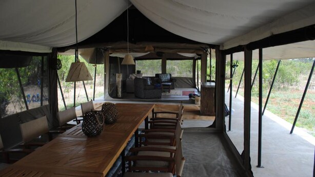 A tented dining area with a wooden table, chairs, and a sofa.