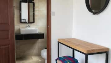 A bathroom with a wooden door, a white sink, a mirror, and a small stool with a plaid blanket.