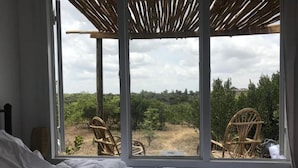 A bedroom with a large window, a bed, and two wicker chairs.