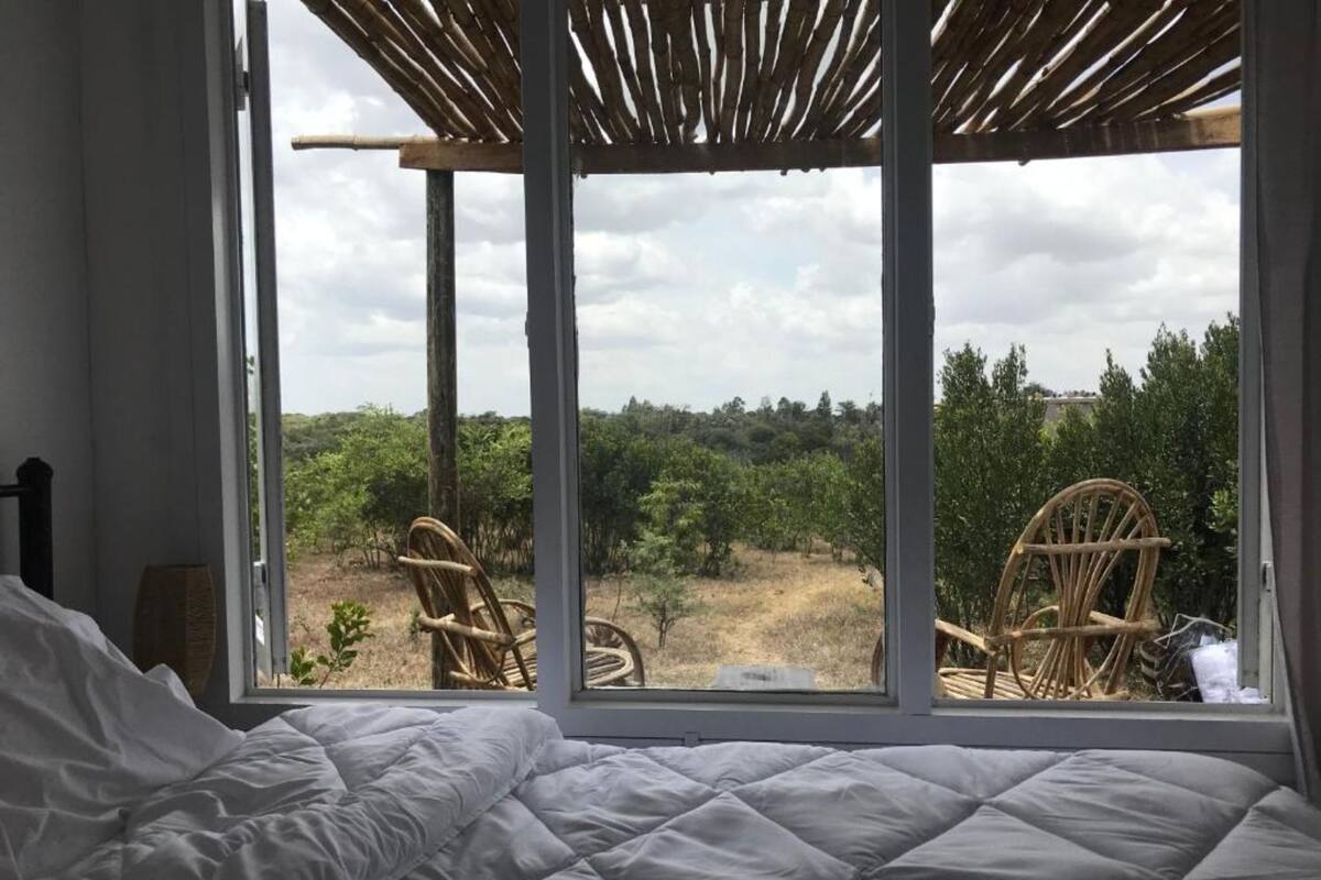 A bedroom with a large window, a bed, and two wicker chairs.