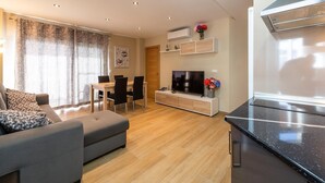 A modern living room with a sofa, a dining table with chairs, a TV, and a kitchen area with a stove. - Apartment "Las góndolas playa" with sea views, shared pool and Wi-Fi (Almunecar)