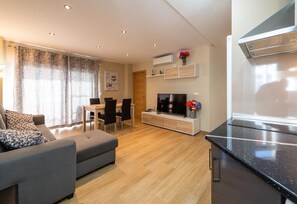 Een moderne woonkamer met een bank, een eettafel met stoelen, een televisie en een keuken met fornuis.
