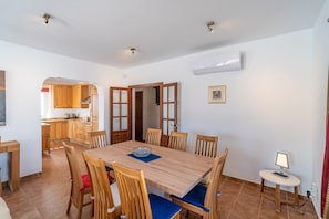 Un comedor con una mesa y sillas de madera, una cocina al fondo y un equipo de aire acondicionado en la pared.