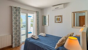 Une chambre d’hôtel comprenant un lit, une lampe de chevet, une fenêtre avec des rideaux, un miroir et un climatiseur fixé au mur.