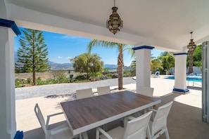 Un espacio cubierto para comer al aire libre con mesa y sillas, una piscina y vistas del paisaje.