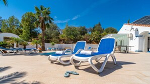 Un espace aménagé au bord de la piscine, avec des chaises longues, une piscine et un bâtiment doté d’un toit en tuiles.