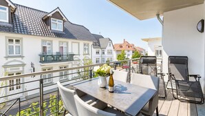 Ein Balkon mit Tisch, Stühlen, einer Blumenvase und einer Weinflasche.