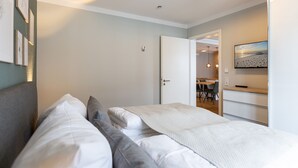 Ein Schlafzimmer mit Bett, Kissen, einem Nachttisch, einem an der Wand montierten Fernseher und einer Tür zu einem Essbereich.