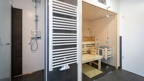 Ein modernes Badezimmer mit Dusche, einer Glaskonstruktion als Sauna und einer Holzbank.