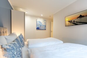 Habitación de hotel moderna con una cama grande, un cuadro de un atardecer sobre el agua y una puerta que da a otra habitación.