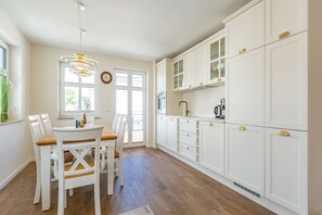 Une cuisine avec des meubles blancs, une table à manger avec des chaises et un luminaire suspendu.