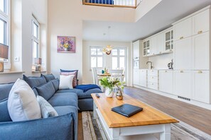 Un salon moderne avec un canapé d’angle, une table basse en bois et un coin repas agrémenté d’un lustre.
