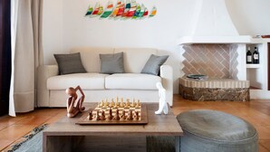 Un salon comprenant un canapé, un jeu d’échecs, une cheminée et une œuvre d’art murale.