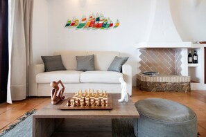 Una sala de estar con un sofá, un tablero de ajedrez, una chimenea y una obra de arte en la pared.