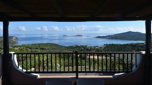 Un balcon offrant une vue sur un paysage côtier, comprenant une étendue d’eau et des collines lointaines.