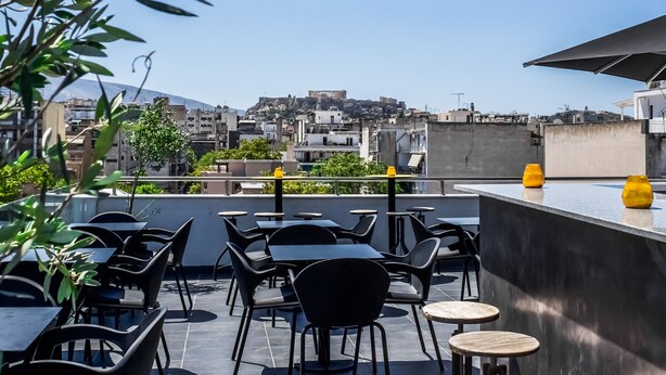 An outdoor seating area with tables and chairs, a view of a cityscape, and a building with a modern design. - Iasonos Suites (Athens)
