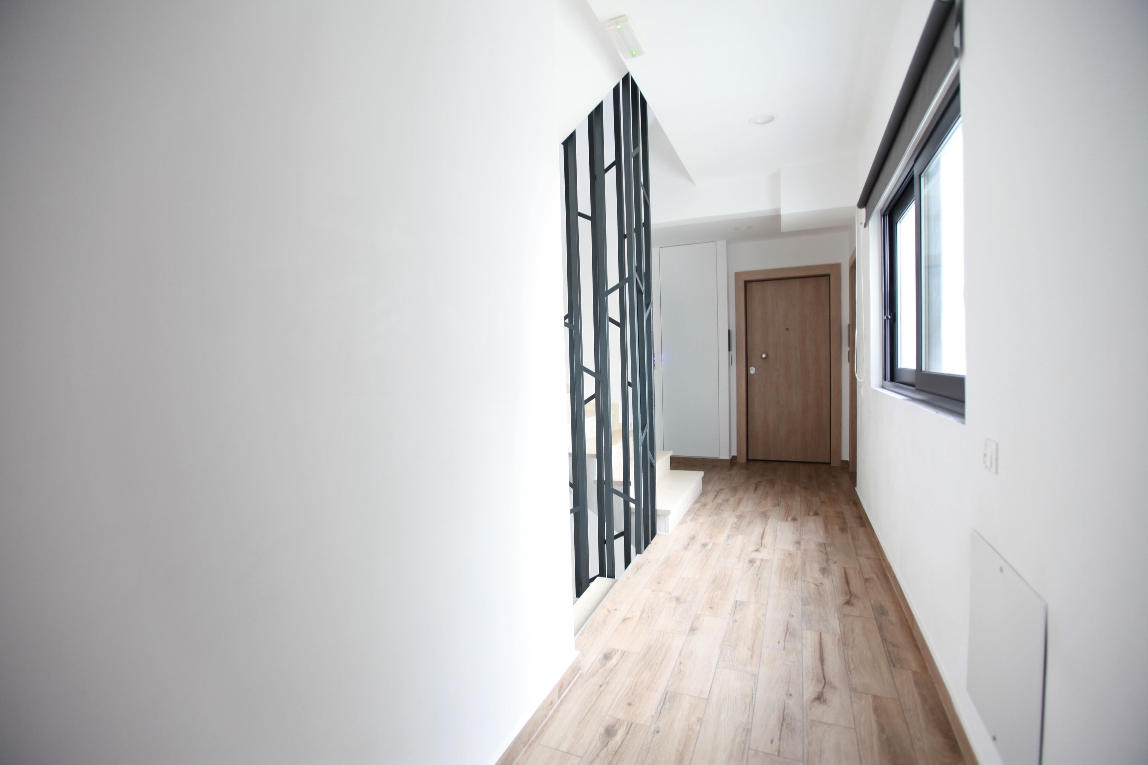 A narrow hallway with wooden flooring and white walls.