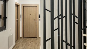 A hallway with a wooden door, a black metal partition, and a light switch on the wall. - Iasonos Suites (Athens)