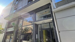 A modern building with a glass facade, a sign for 'FAMAKER' on the ground floor, and a 'FASONOS SUITES' sign above the entrance. - Iasonos Suites (Athens)