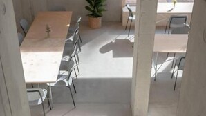 Una escalera conduce a un comedor con mesas y sillas, una planta en maceta y vistas al exterior.