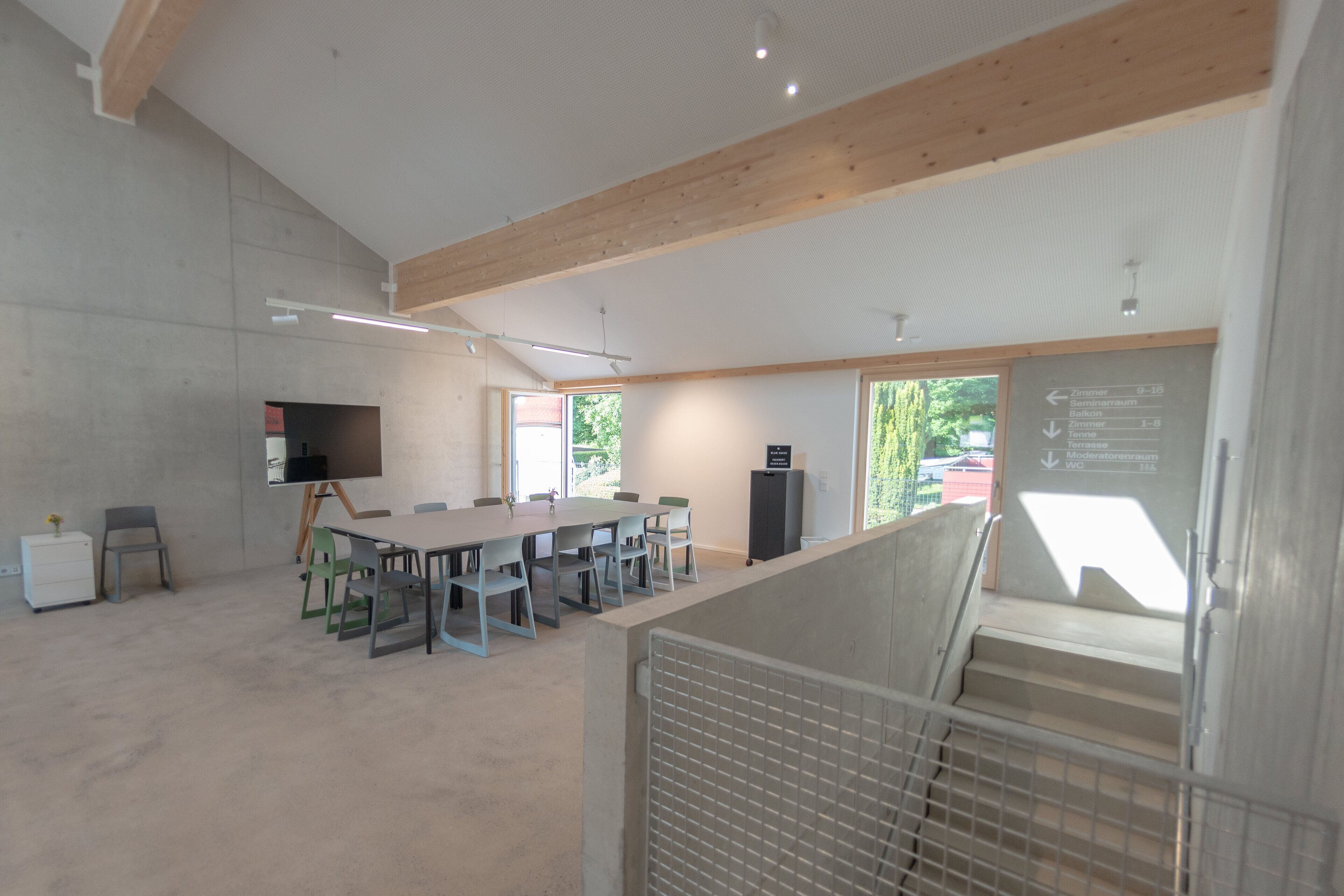A spacious conference room with a long table, chairs, a projector, and a whiteboard with directional signs.
