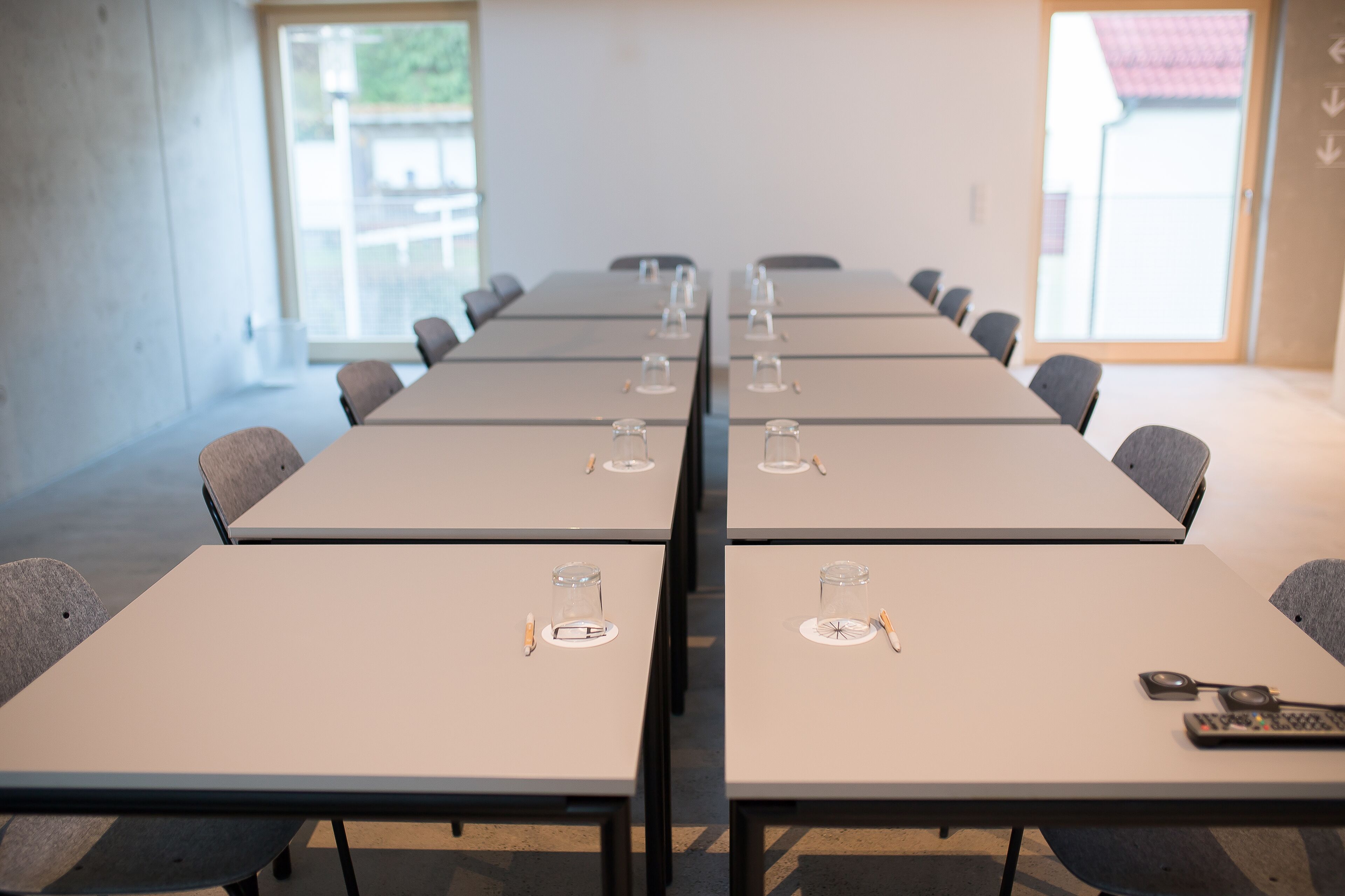 A conference room with long tables, chairs, and a window with a view of a building.