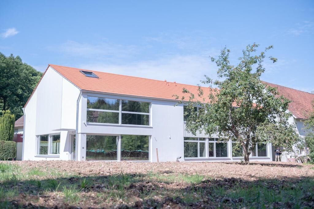 Ein modernes, zweistöckiges Haus mit großen Fenstern und einem roten Ziegeldach.