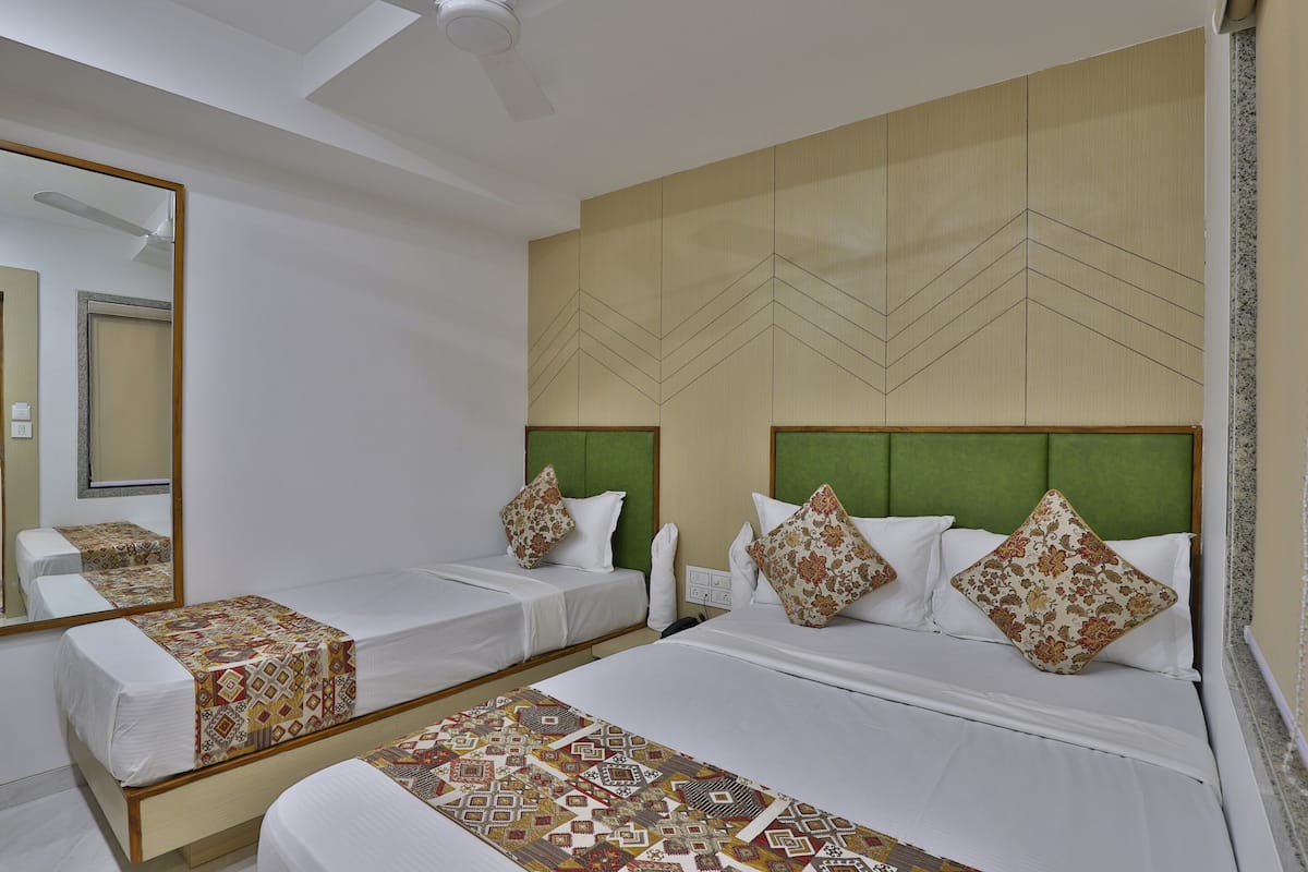 A hotel room with two single beds, a large mirror, and a green headboard.