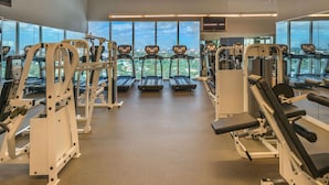 A gym with treadmills, weight machines, and large windows offering a city view.