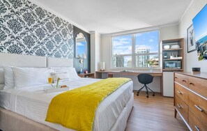 A modern hotel room with a large bed, a desk, and a view of the cityscape.