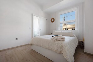 A bedroom with a bed, a window, a door, and a small table.