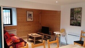 A cozy living room with a wooden wall, a sofa, a coffee table, a TV, and a chair. - 2 Bedroom Private vacation home in Soueix-Rogalle (Soueix-Rogalle)