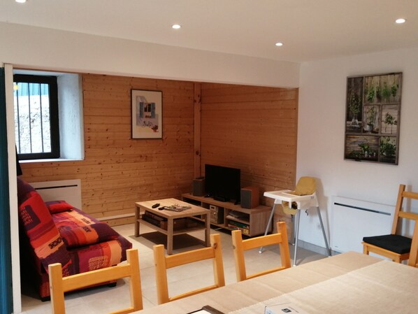 A cozy living room with a wooden wall, a sofa, a coffee table, a TV, and a chair.