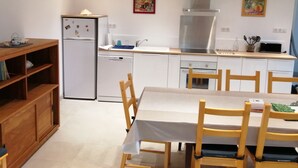 A compact kitchen with white cabinets, a stainless steel range hood, and a dining area with a table and chairs. - 2 Bedroom Private vacation home in Soueix-Rogalle (Soueix-Rogalle)