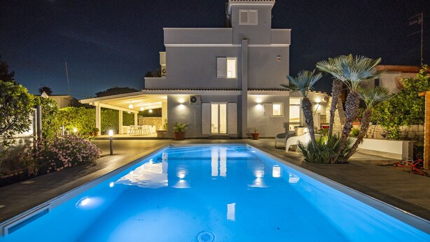 Ett modernt hus med en swimmingpool, utomhusmöbler och en väl upplyst uteplats.