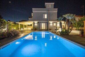 A modern house with a swimming pool, outdoor seating, and a well-lit patio area.
