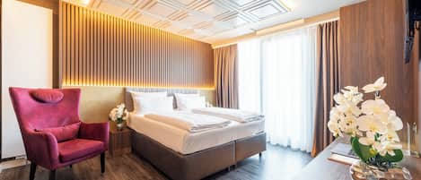 Una habitación de hotel moderna con una cama grande, un sillón rojo, un cabecero de madera y un jarrón decorativo con orquídeas.