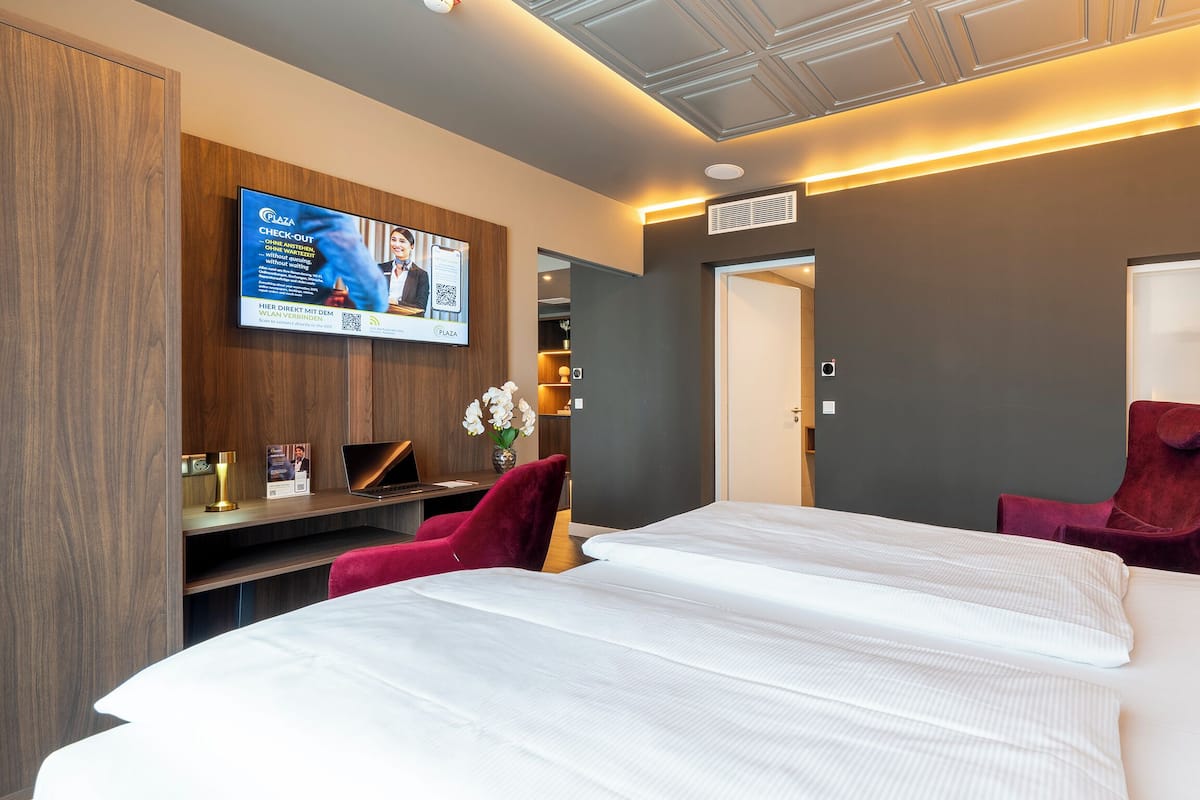 A hotel room with a bed, a desk with a laptop, a TV, and a red chair.